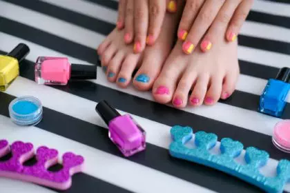 Childrens feet with bright pedicure and manicure of colors and bottles of bright nail polish.